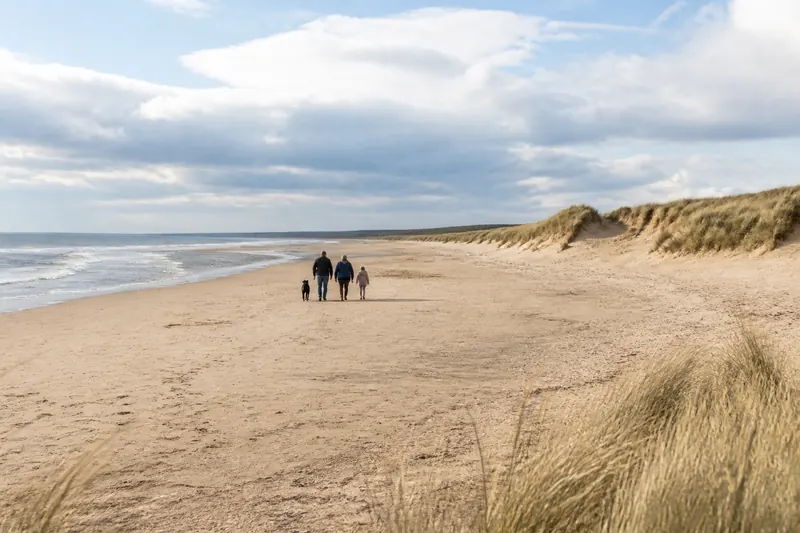 A wide sandy beach with dunes and walkers in the distance