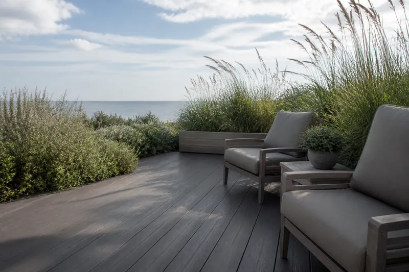 A grey composite deck with chairs and grasses by the sea